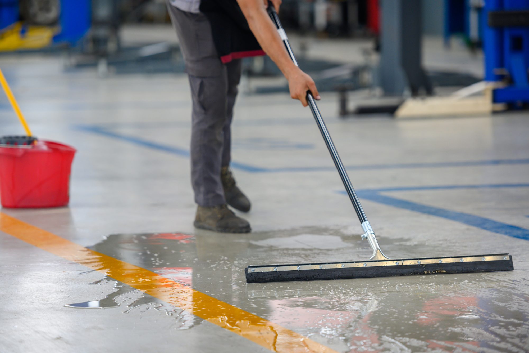 Car mechanic cleaning the garage floor at the auto industry shop workshop Use a mop to clean water from the epoxy floor in the car repair center.